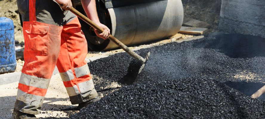 A Sable Asphalt paving team member spreads asphalt on to the ground.